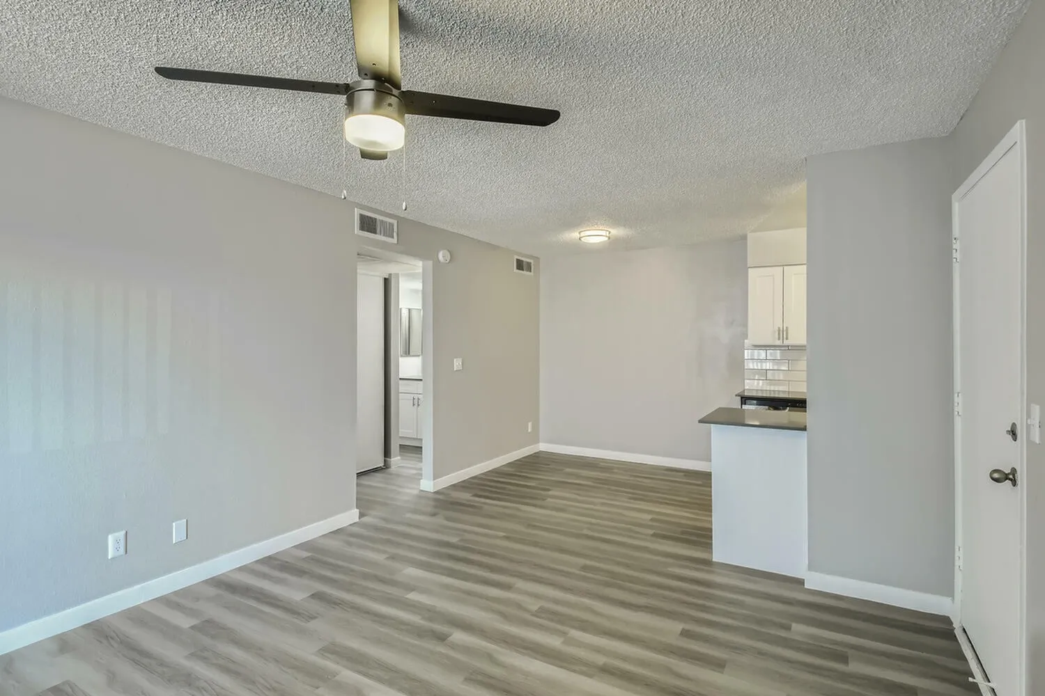 Open living area, wood-style plank flooring, ceiling fan, white cabinetry