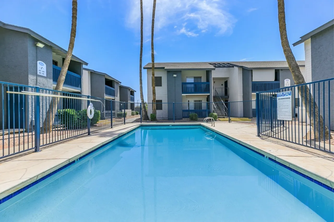 Swimming pool, metal railing fence, apartment buildings, palm trees, clear blue sky