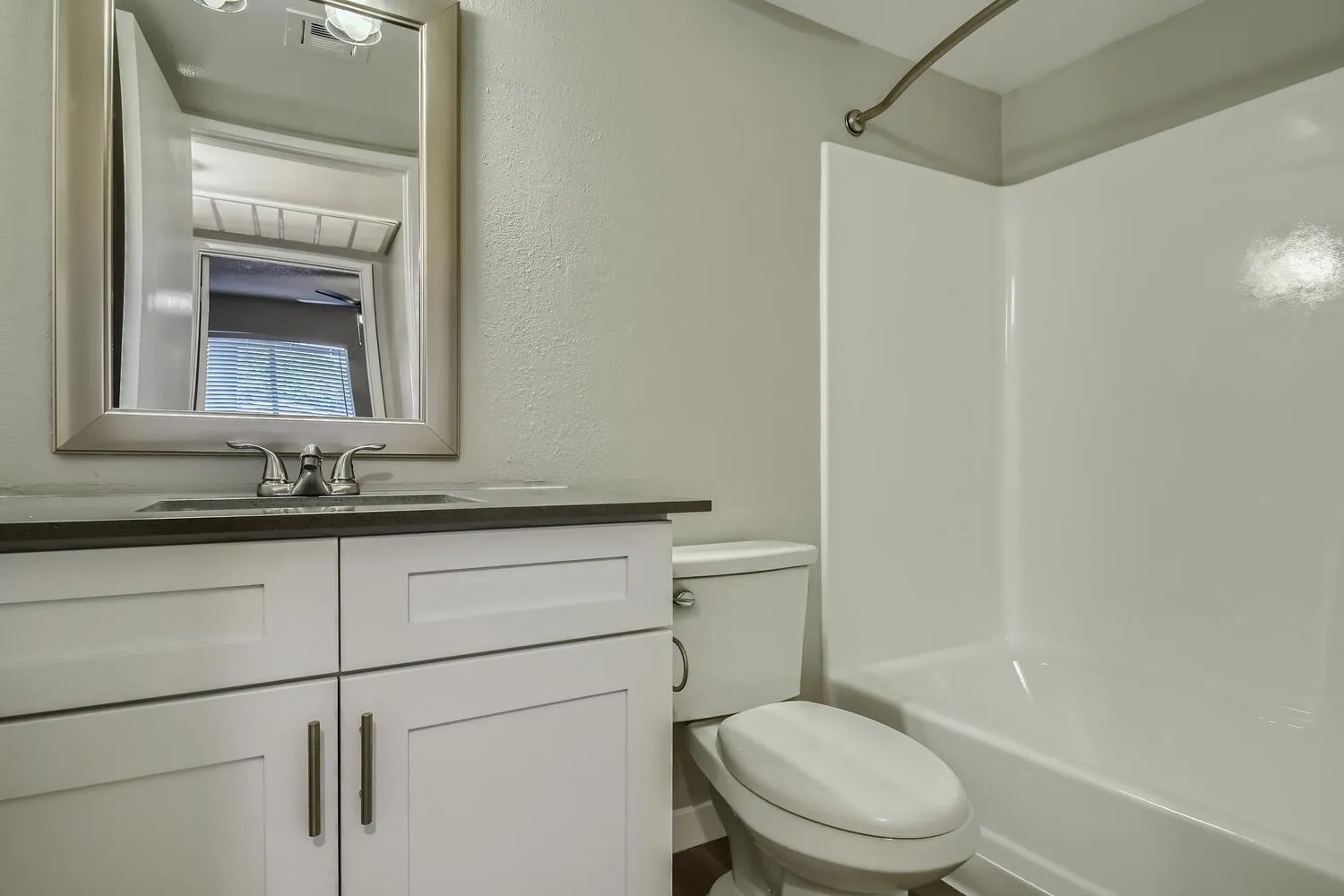 Bathroom, white vanity cabinetry, dark countertop, framed mirror, toilet, shower enclosure