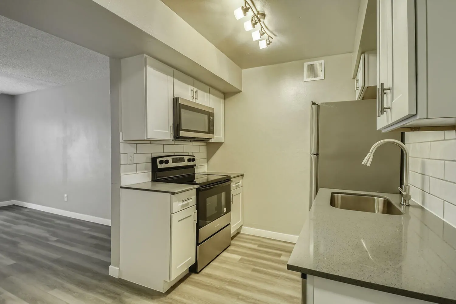 Kitchen, white shaker cabinetry, black countertops, stainless steel appliances, subway tile backsplash, wood-style plank flooring