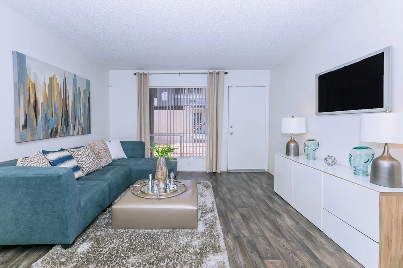 Living room, teal sofa, wood-style plank flooring, area rug, mounted TV, patio door
