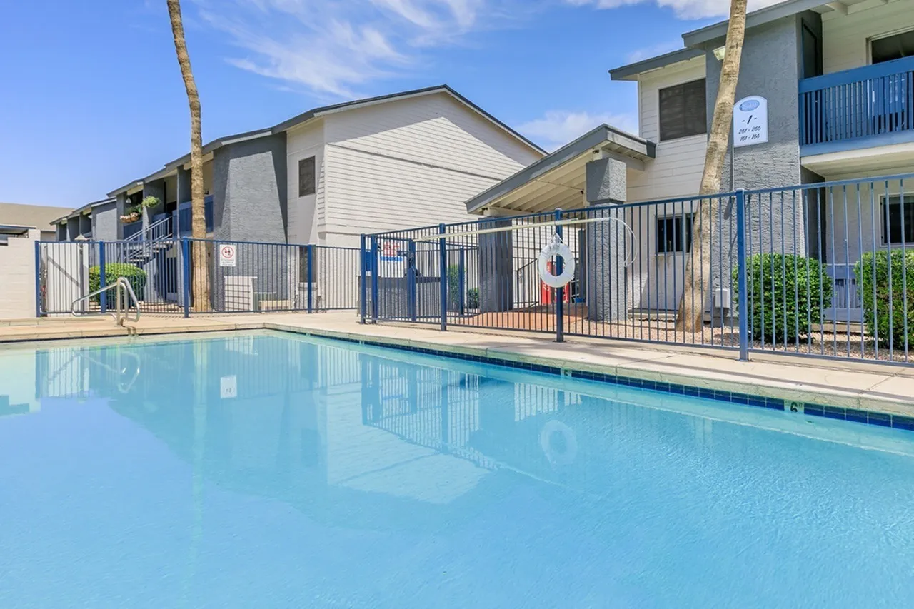 Community pool, metal railing fence, residential buildings, palm trees, clear blue water