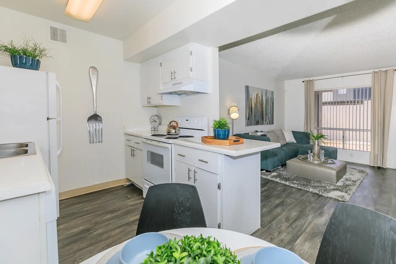 Kitchen and dining area, white cabinetry, quartz countertops, stainless steel appliances, wood-style plank flooring, living room with seating visible