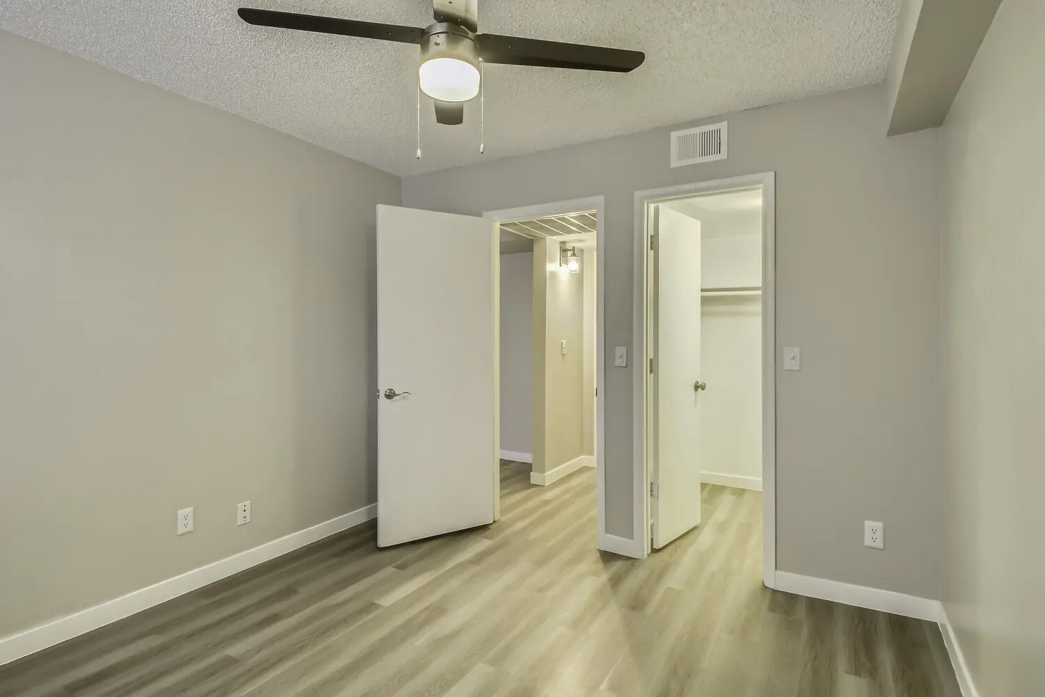 Primary bedroom, wood-style plank flooring, ceiling fan with light, dual closet doors, ensuite bathroom entry
