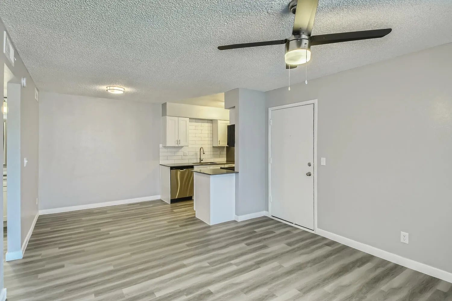 Kitchen and living area, wood-style plank flooring, white cabinetry, ceiling fan