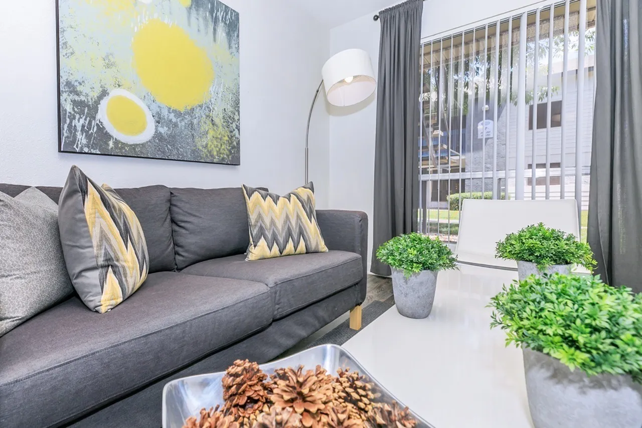Living room, gray sofa with yellow accent pillows, arc floor lamp, potted green plants
