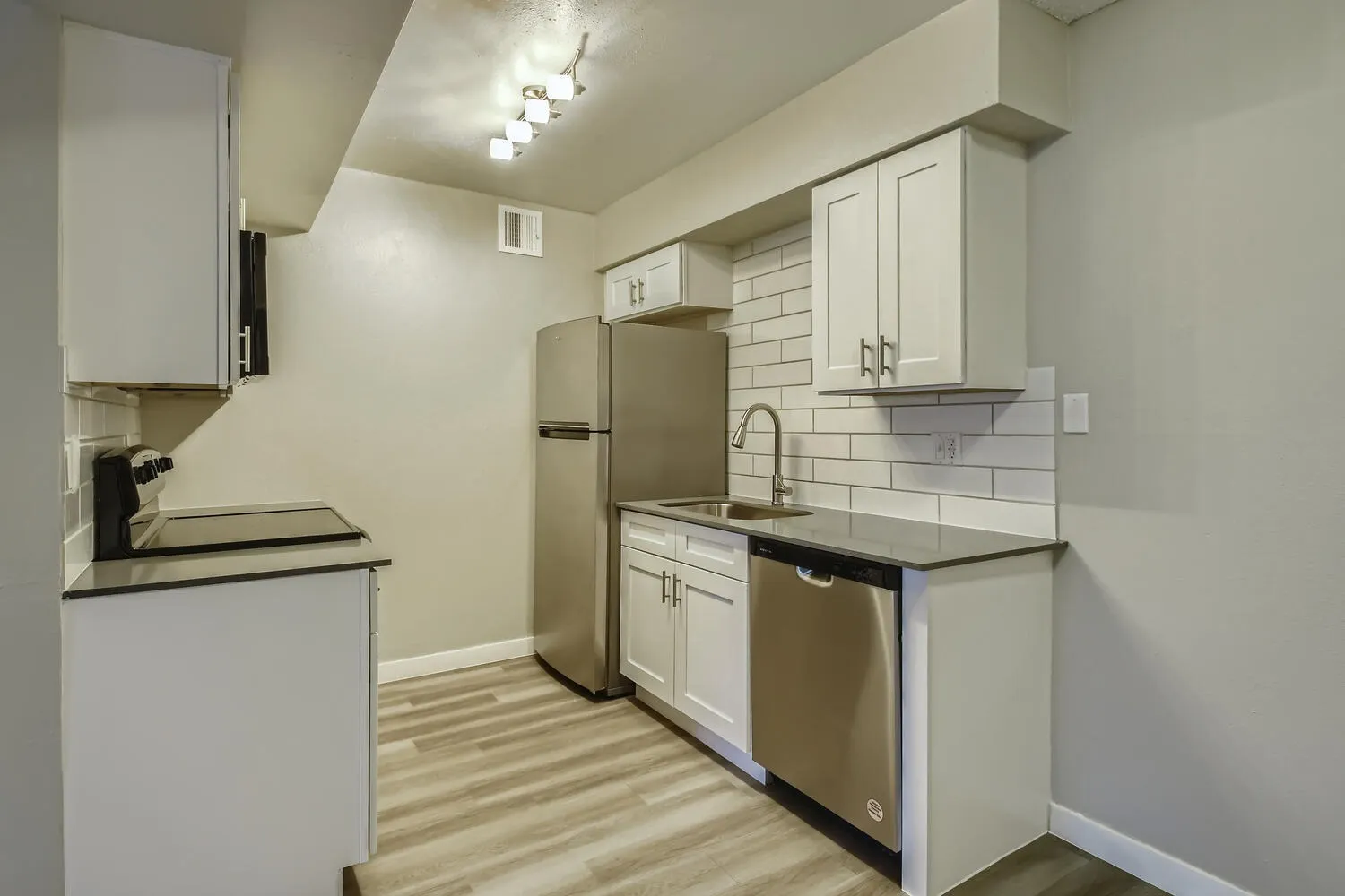 Kitchen, white shaker cabinetry, black countertops, stainless appliances, subway tile backsplash, wood-style plank flooring