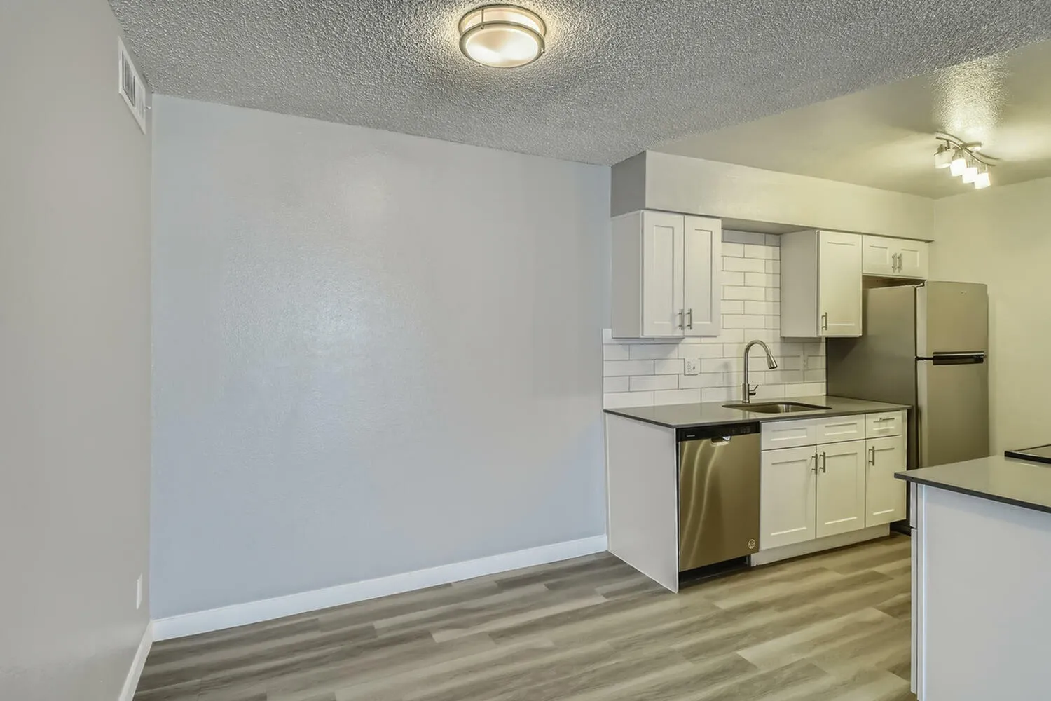 Kitchen, white shaker cabinetry, black countertops, stainless appliances, wood-style plank flooring