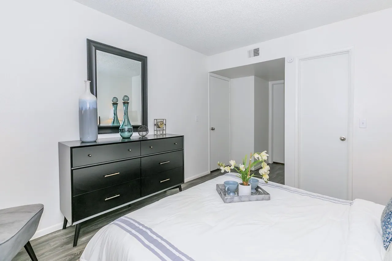 Primary bedroom, black dresser with mirror, white bedding, wood-style plank flooring