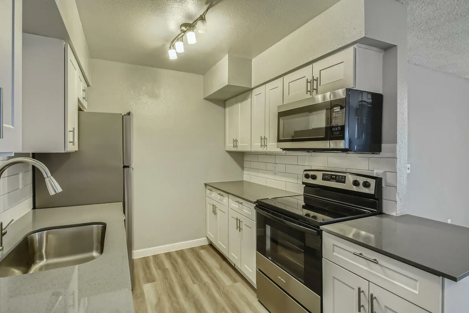 Kitchen, white shaker cabinetry, black countertops, stainless steel appliances, wood-style plank flooring