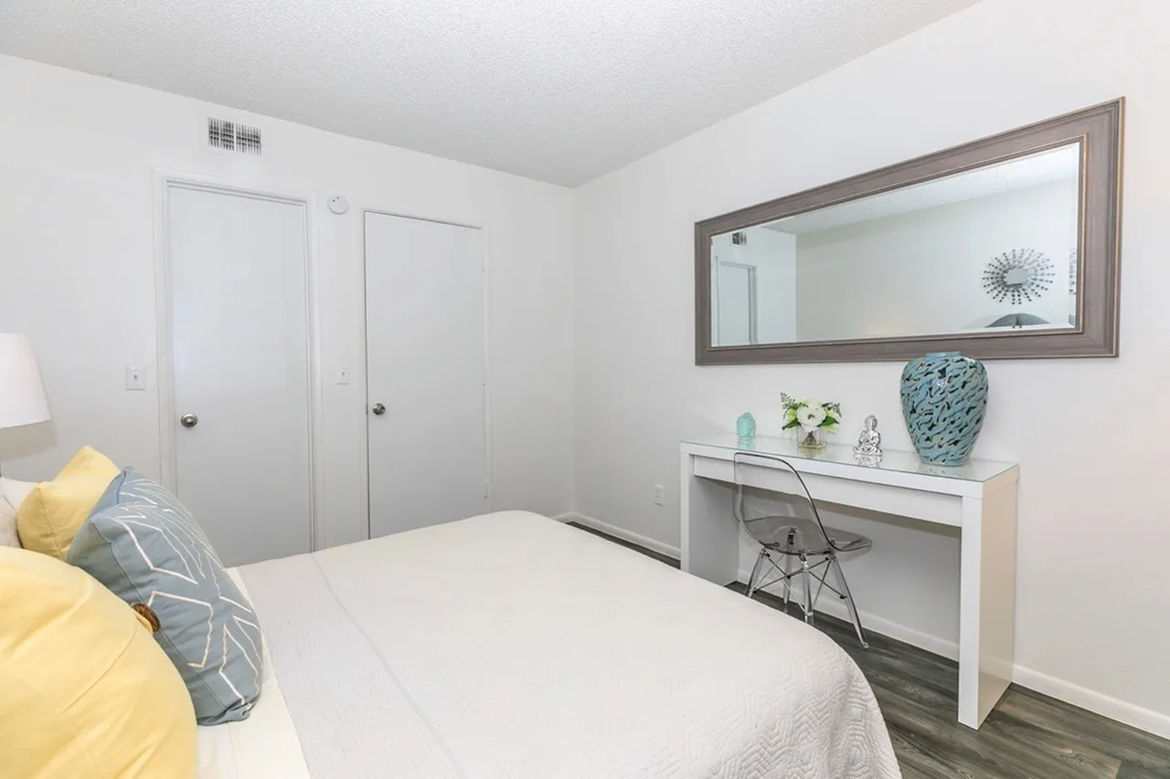 Primary bedroom, white bedding, wood-style plank flooring, vanity with mirror