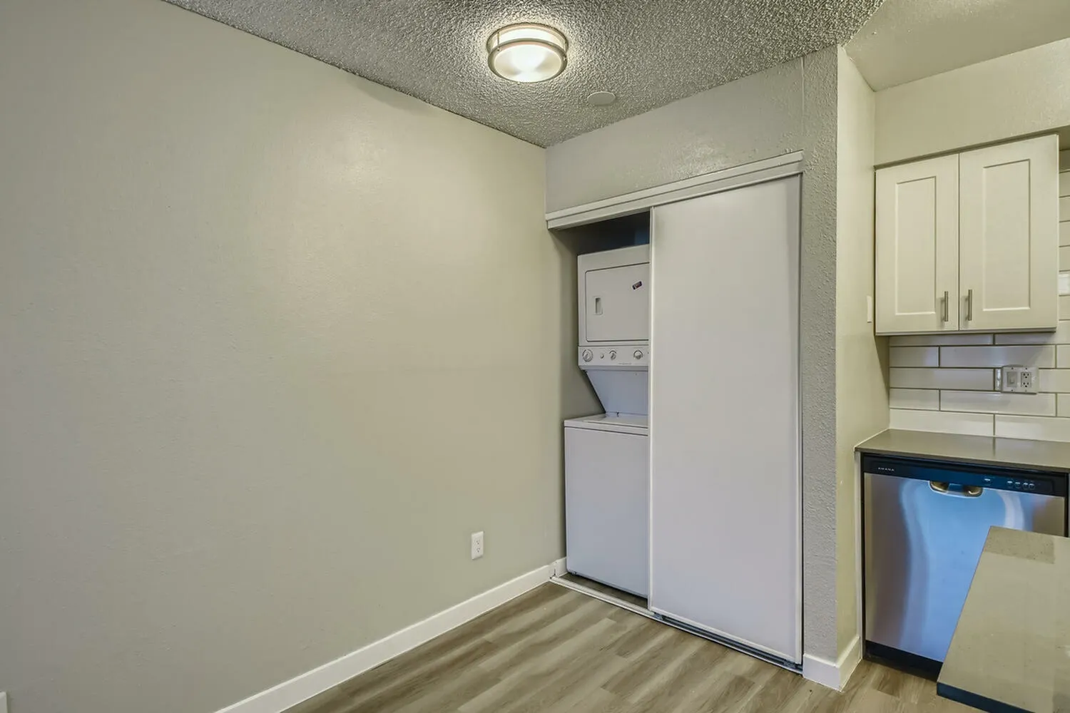 Kitchen area, white cabinetry, subway tile backsplash, stainless appliances, wood-style plank flooring, stacked washer dryer