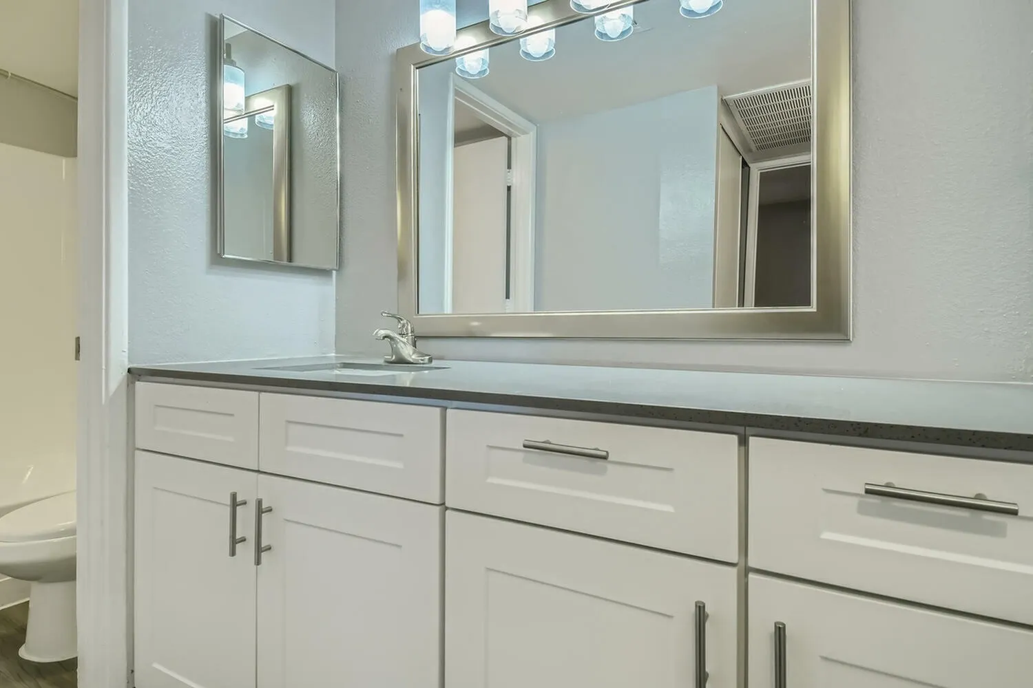 Primary bathroom, white shaker cabinetry, quartz countertop, framed mirror, brushed nickel hardware