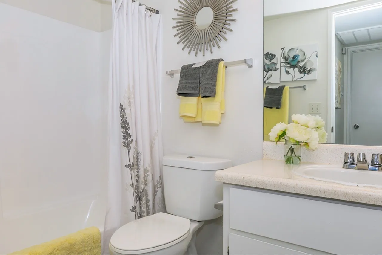 Bathroom, white cabinetry, quartz countertop, yellow towels, sunburst mirror