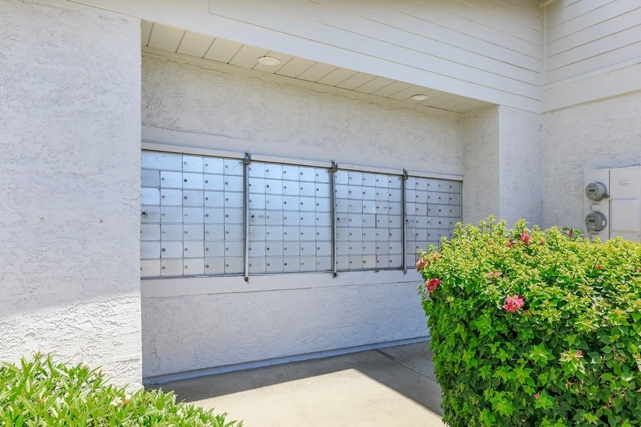 Mailroom, wall-mounted metal mailboxes, concrete walls, flowering shrub accent