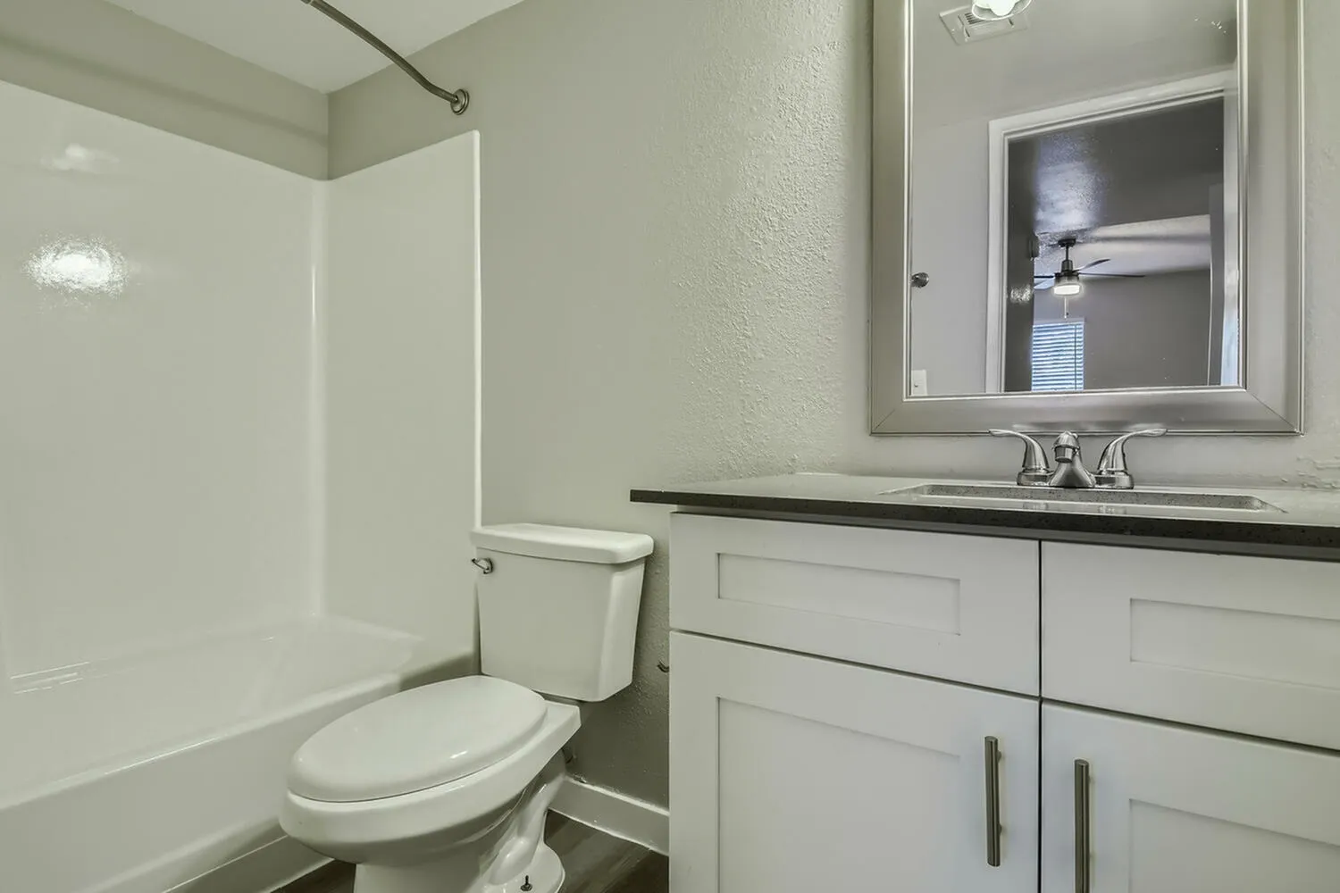Bathroom, white vanity with black countertop, framed mirror, toilet, tile shower