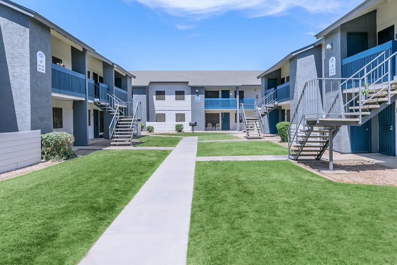 Courtyard with green lawn, concrete walkway, multi-story residential building, blue railings, exterior stairs