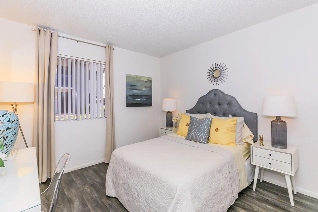 Primary bedroom, gray upholstered headboard, wood-style plank flooring, yellow accent pillows