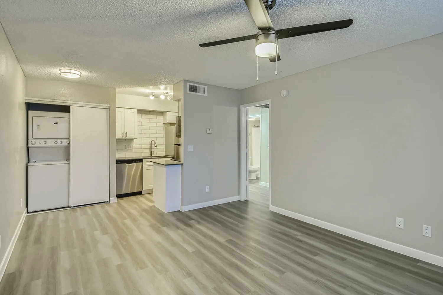 Living room and kitchen, wood-style plank flooring, ceiling fan, stainless appliances, white cabinetry