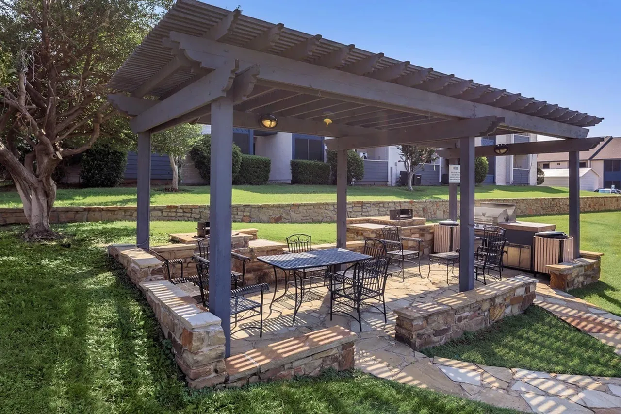Covered patio with stone columns, pergola roof, dining tables and chairs, mature tree