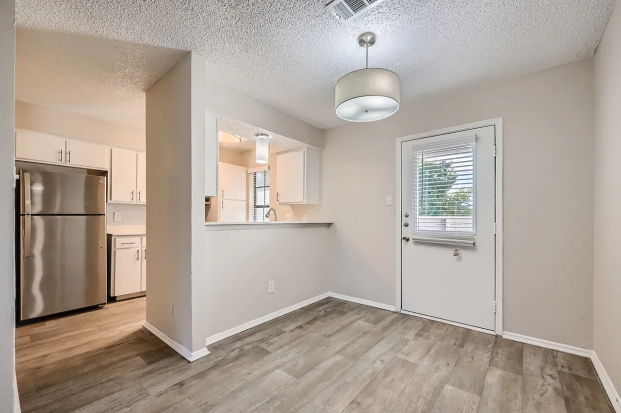 Kitchen with stainless appliances and cream cabinetry, dining area with wood-style plank flooring, pendant lighting