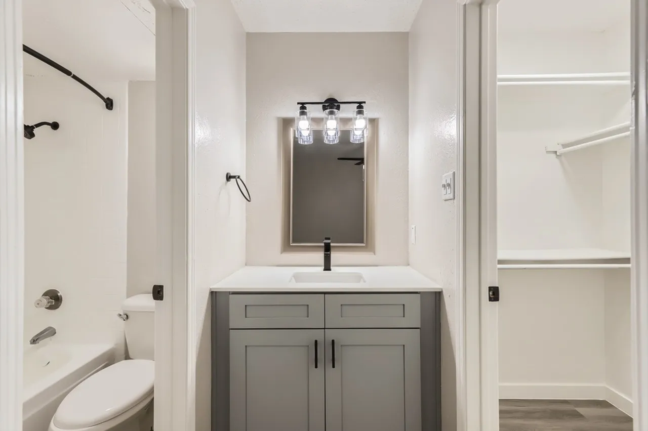 Primary bathroom, gray cabinetry, white quartz countertop, black faucet, framed mirror, vanity lighting