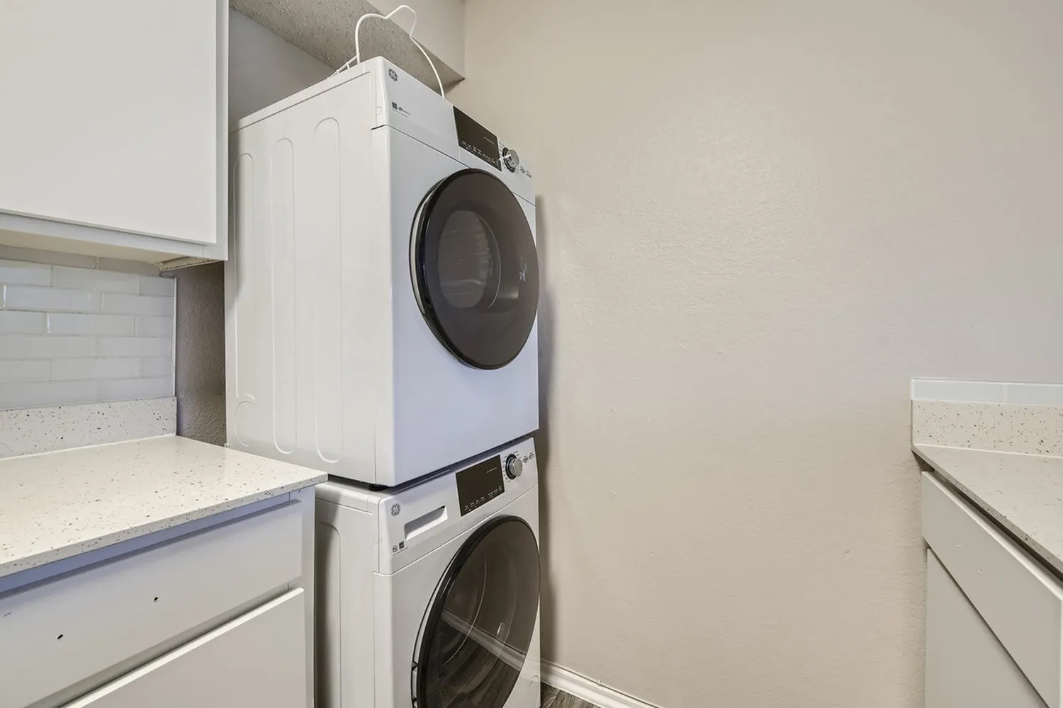 Laundry room, stacked white washer and dryer, light countertop, cabinetry