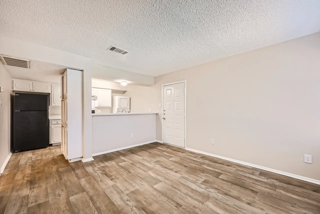 Kitchen and living space, wood-style plank flooring, white cabinetry, black refrigerator, white counter divider