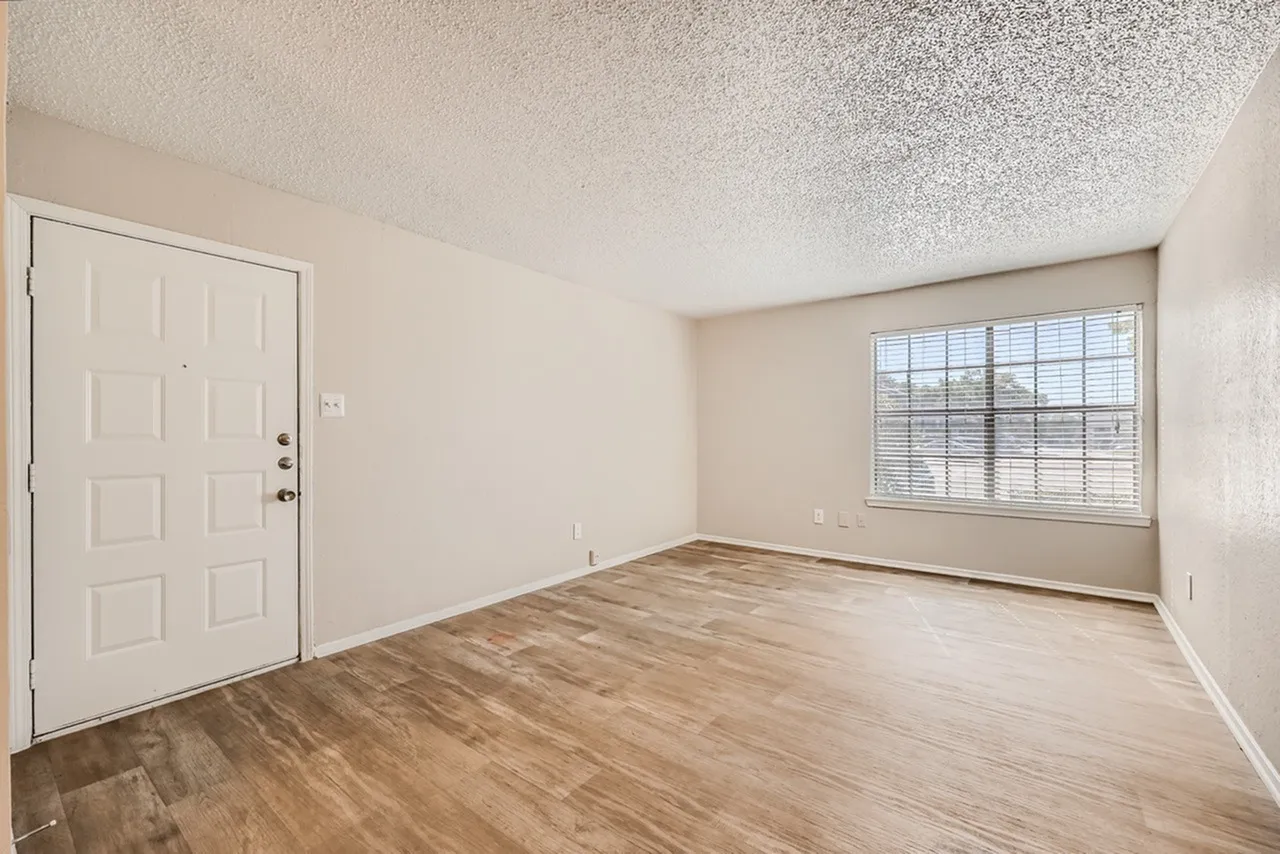 Living room, wood-style plank flooring, entry door, large window, textured ceiling