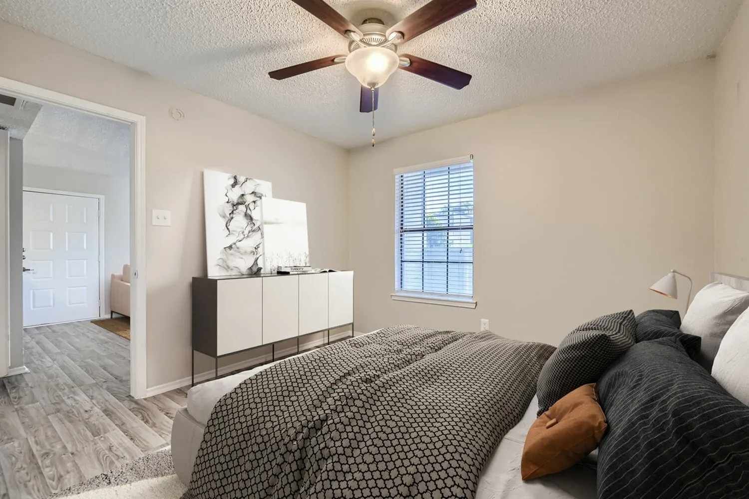 Primary bedroom, wood-style plank flooring, ceiling fan with light fixture, white dresser with artwork