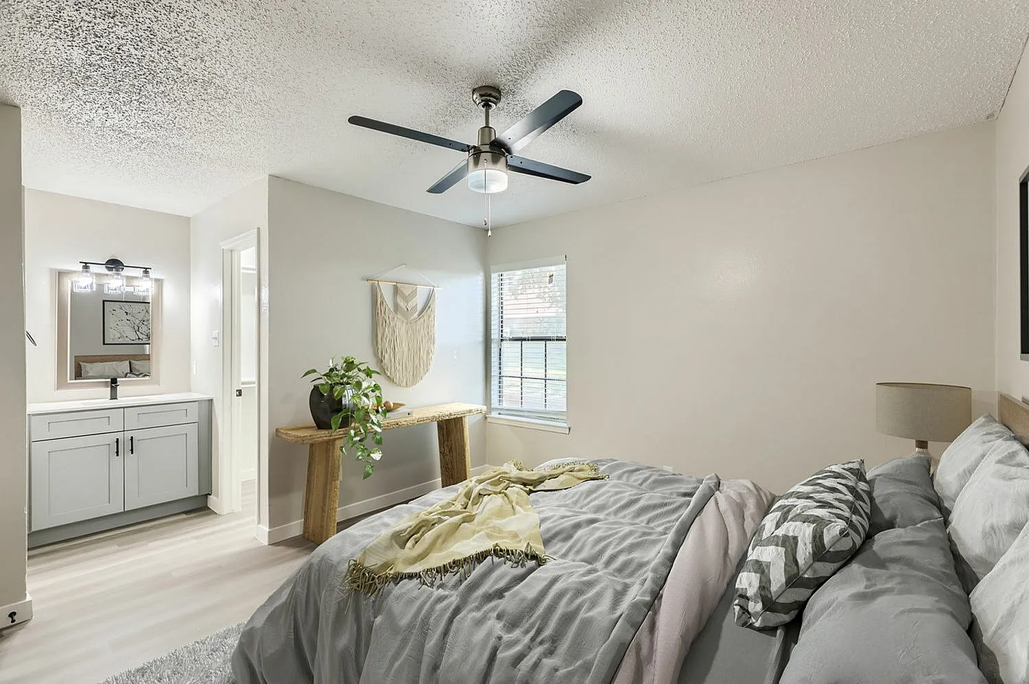 Primary bedroom, gray bedding, wood-style plank flooring, ceiling fan, ensuite bathroom visible