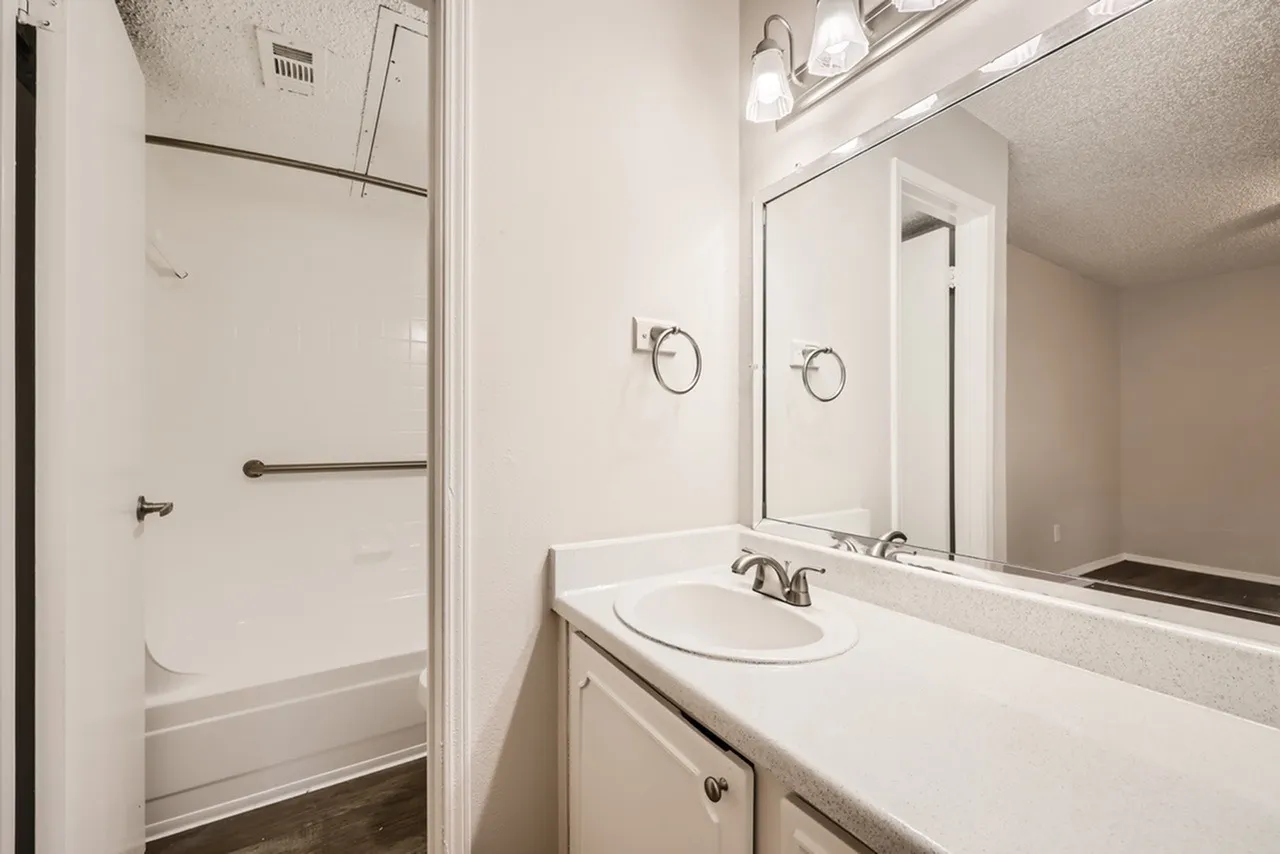 Bathroom, white vanity with round sink, large mirror, white tile shower enclosure, overhead lighting