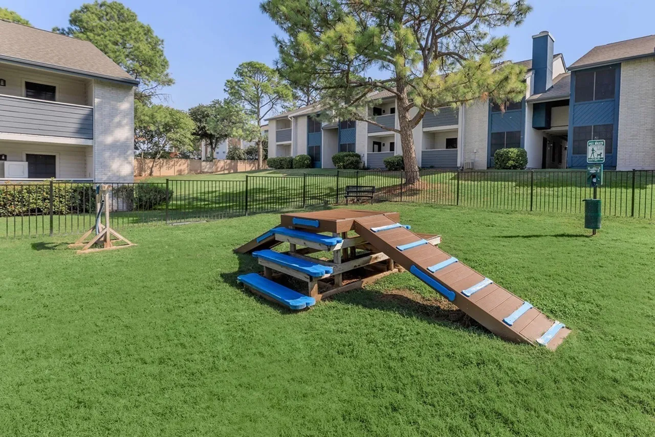 Community lawn with cornhole game setup, apartment buildings, green grass, mature trees
