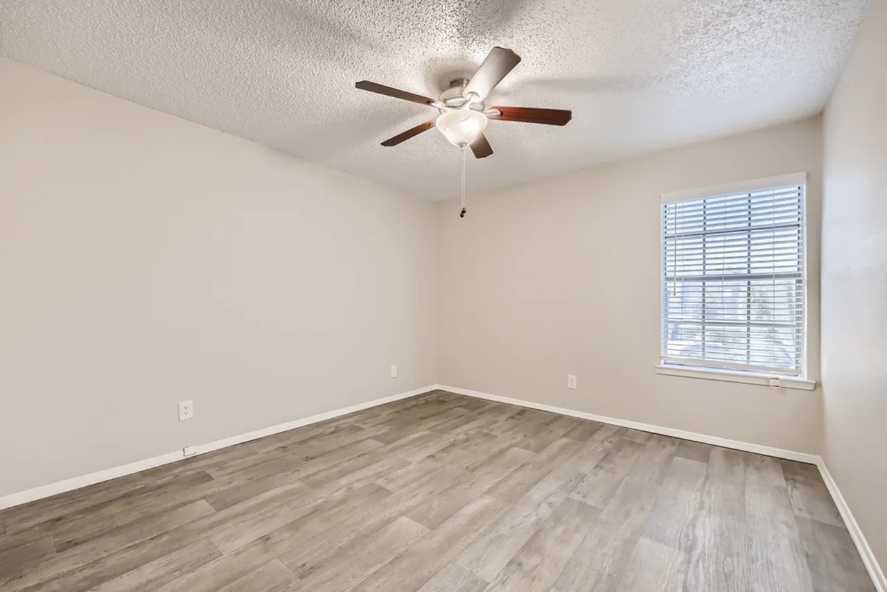 Bedroom, wood-style plank flooring, ceiling fan with light, window with shutters, textured ceiling