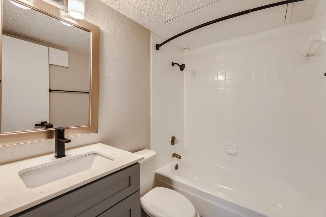 Bathroom, white undermount sink, dark vanity cabinetry, framed mirror, white subway tile shower surround
