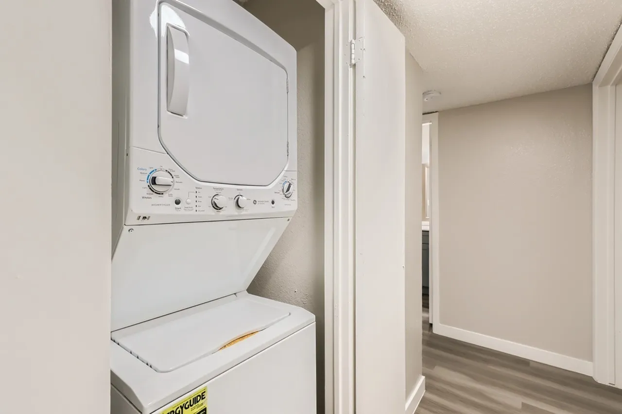 Laundry closet with stacked white washer and dryer, wood-style plank flooring