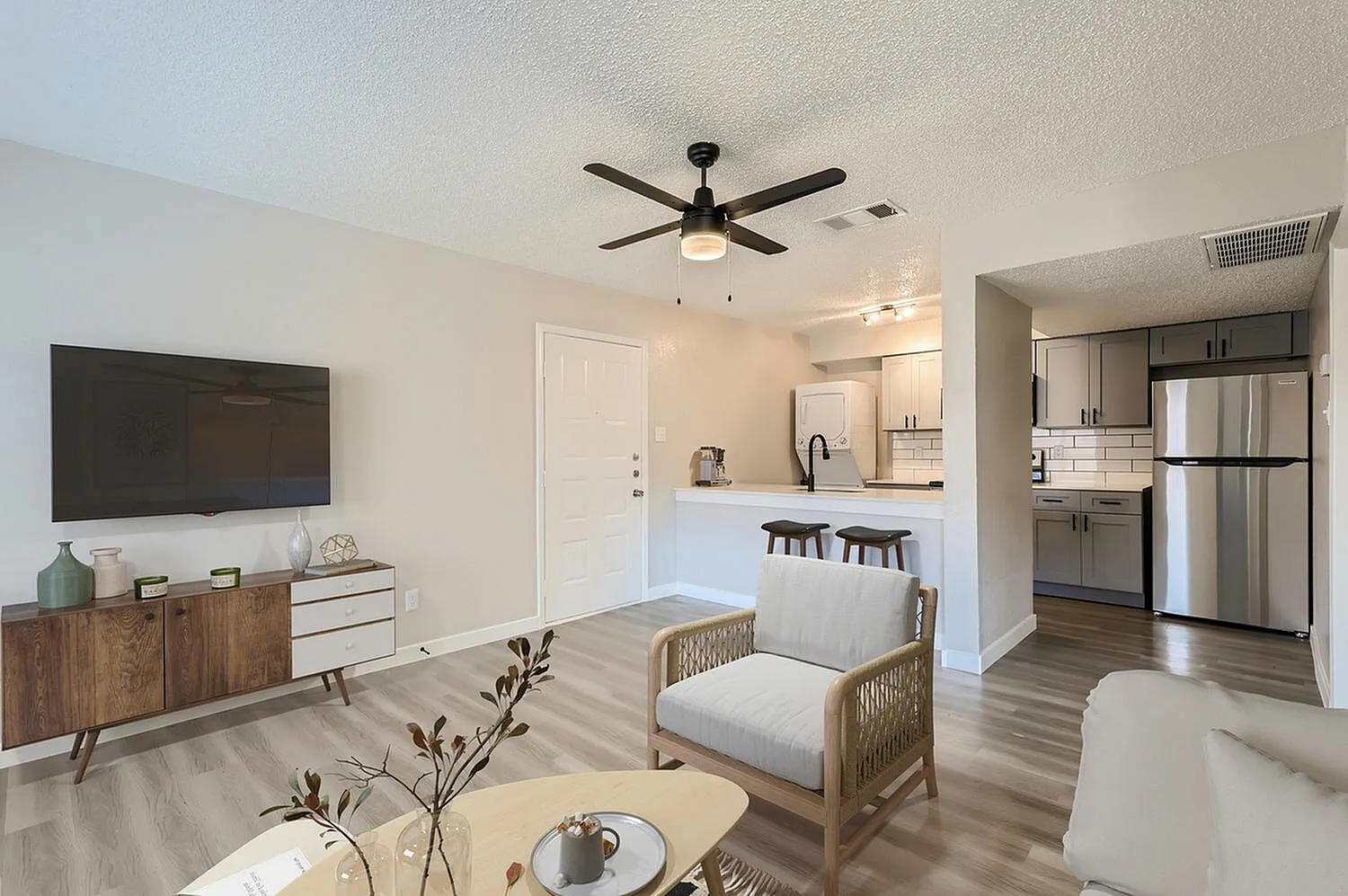 Living room and kitchen, wood-style plank flooring, ceiling fan, gray upholstered chair, stainless appliances