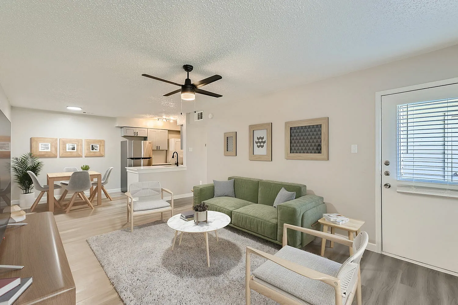 Living room with green sofa, wood-style plank flooring, ceiling fan, white round coffee table, dining area, stainless appliances