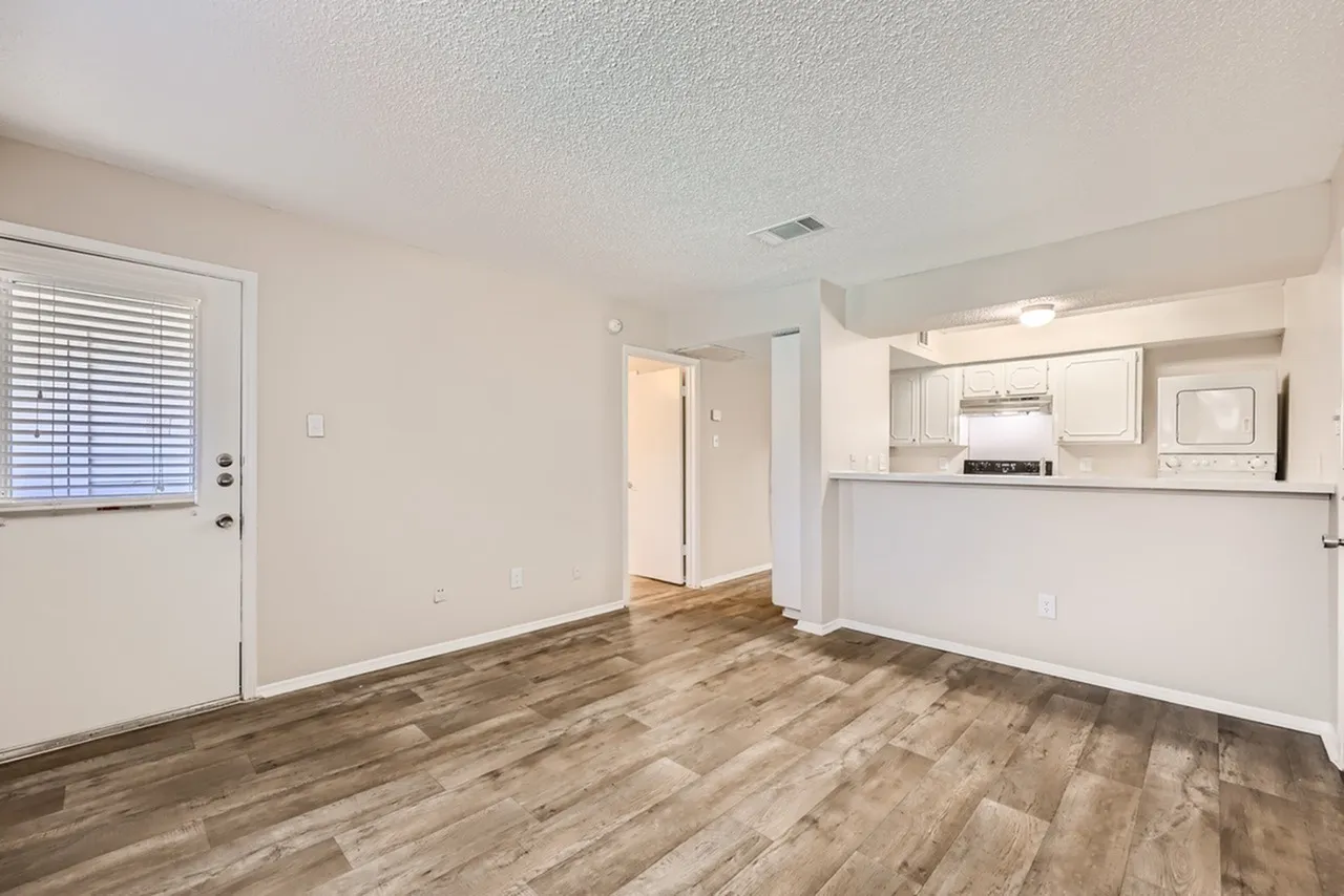 Living room and kitchen area, wood-style plank flooring, white cabinetry, stainless appliances