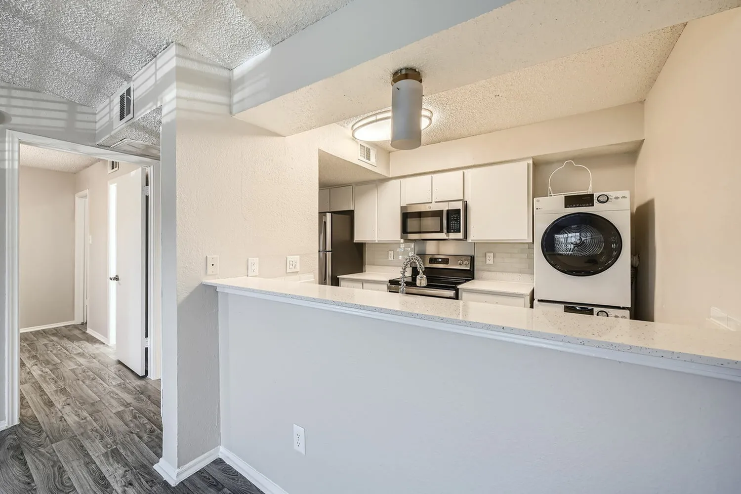 Kitchen with white cabinetry, stainless appliances, quartz countertops, wood-style plank flooring