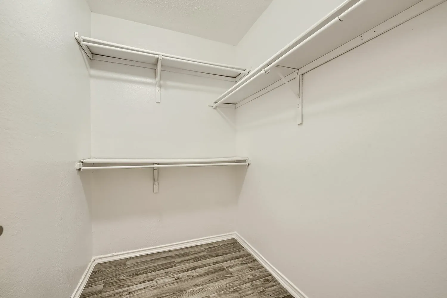 Walk-in closet, metal hanging rods, shelving, wood-style plank flooring