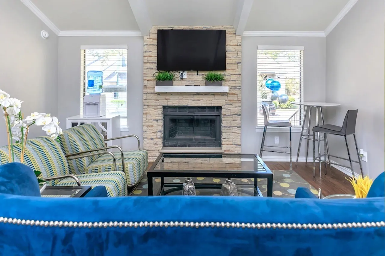 Living room, stone fireplace with mounted TV, striped accent chairs, wood-style plank flooring, glass doors with shutters