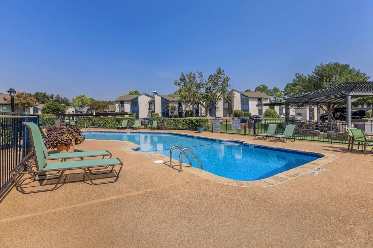 Pool area, lounge chairs, concrete deck, mature landscaping, metal fencing