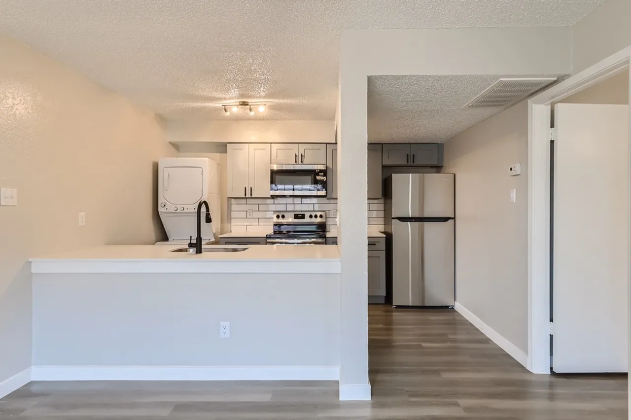 Kitchen with white cabinetry, stainless appliances, quartz countertop, wood-style plank flooring, entry door