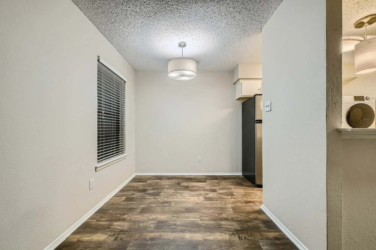 Living space, wood-style plank flooring, white walls, pendant light fixture, vent register