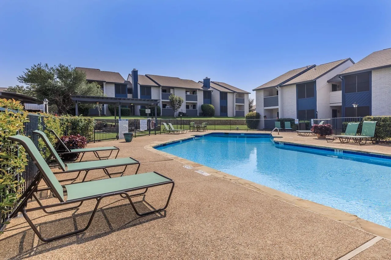 Swimming pool with lounge chairs, concrete deck, apartment buildings, landscaping