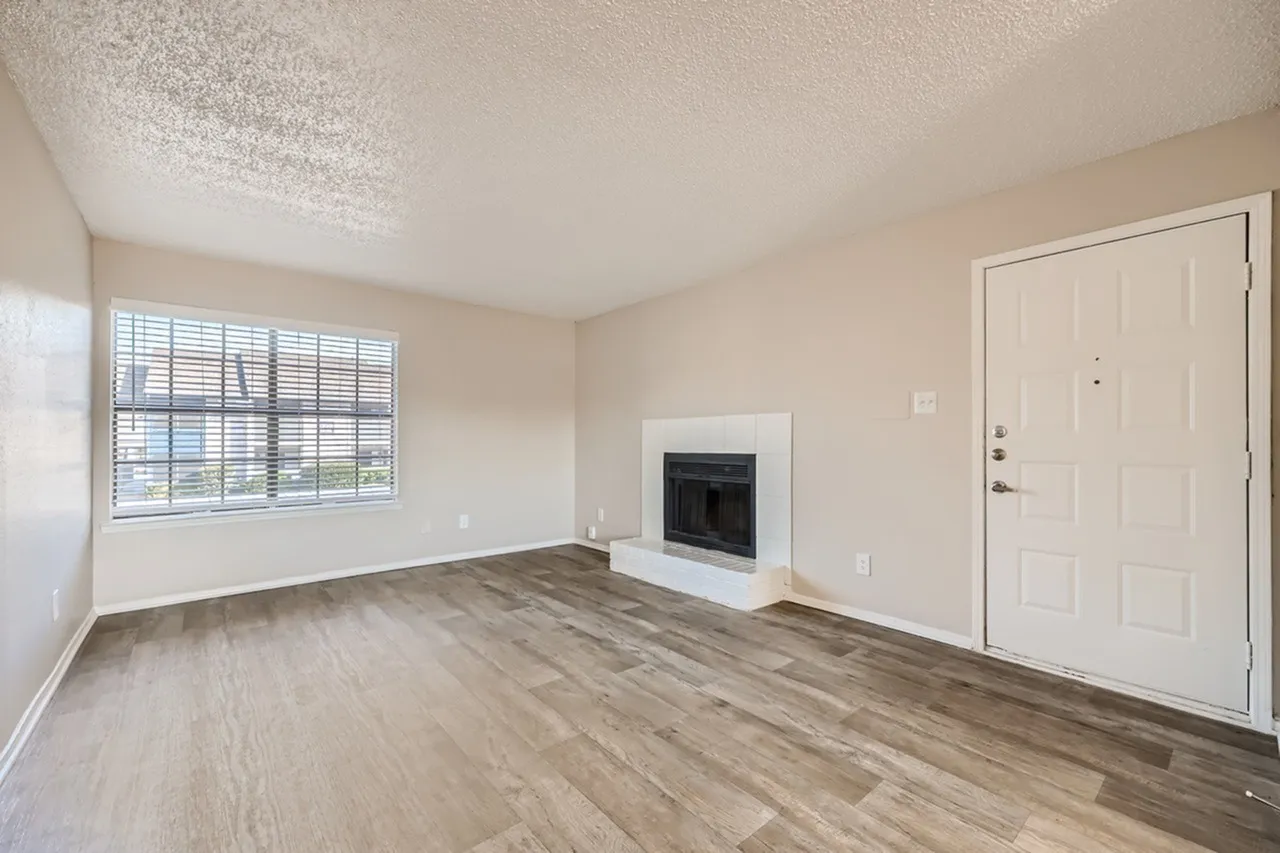 Living room, wood-style plank flooring, white fireplace, large window, white entry door