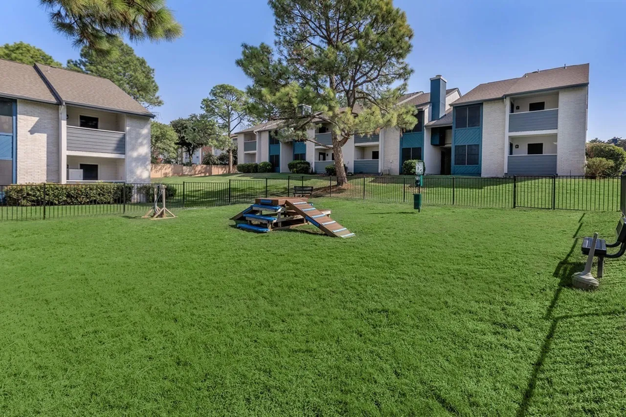 Community lawn, residential buildings, play structures, large trees, metal fencing