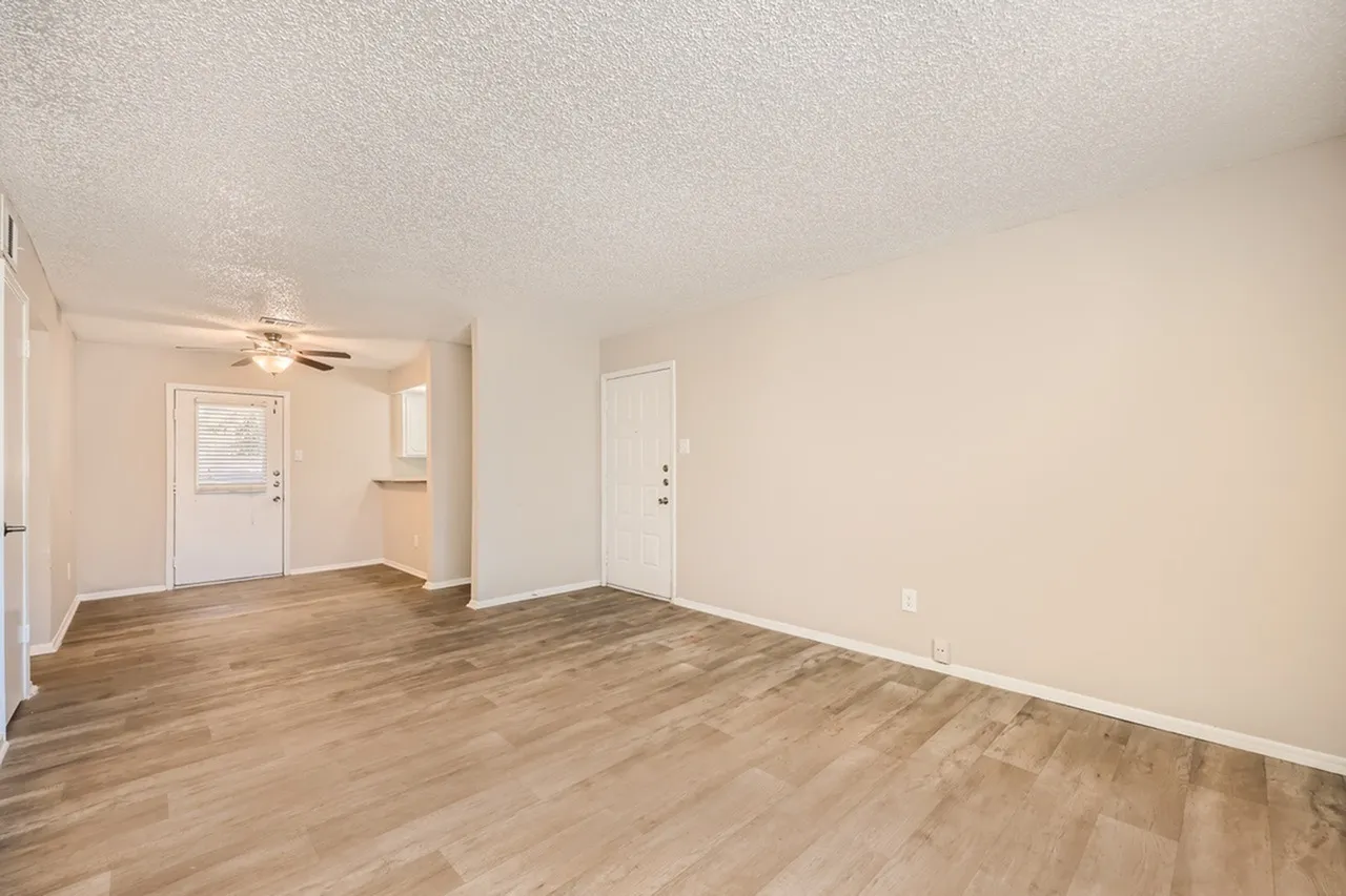 Living room with wood-style plank flooring, ceiling fan, white entry door, open floor plan