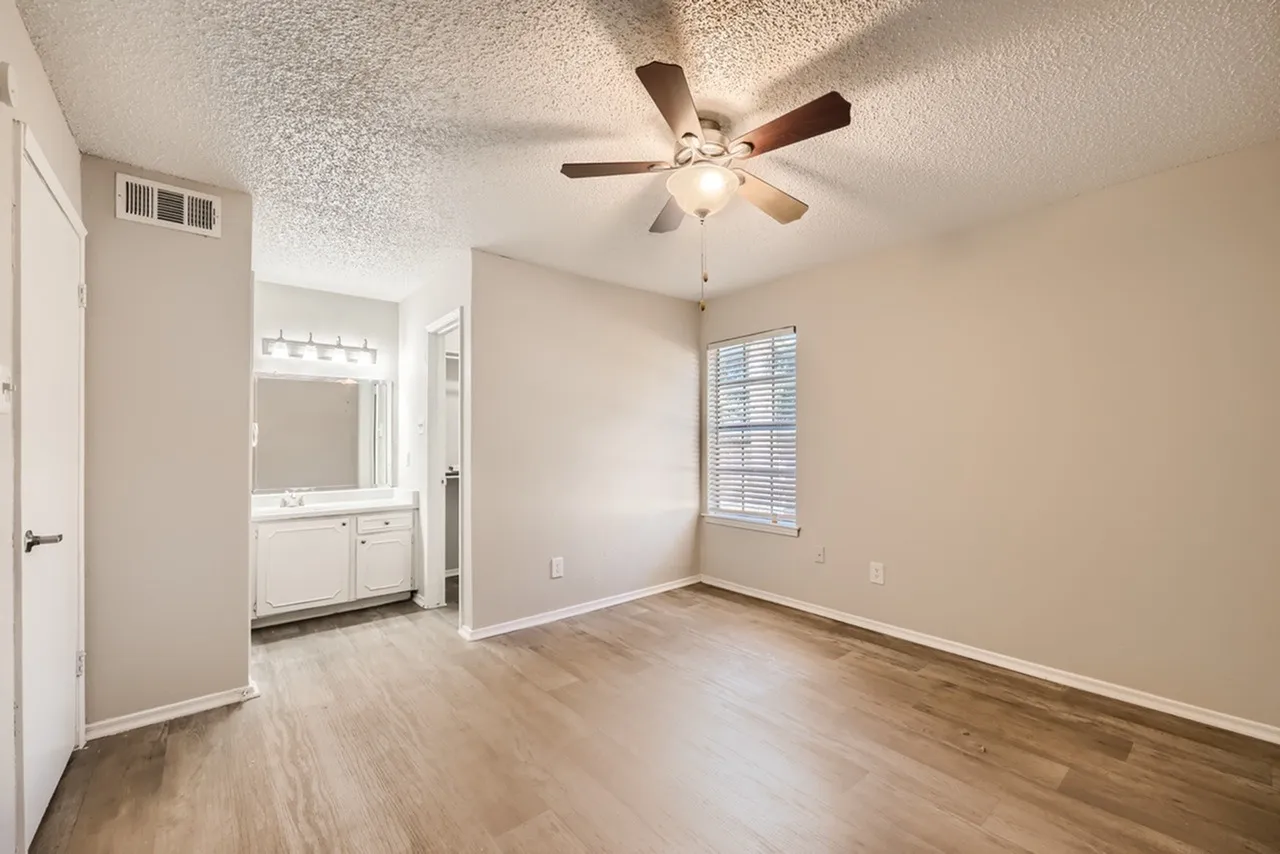Primary bedroom, wood-style plank flooring, ceiling fan with light, ensuite bathroom entry